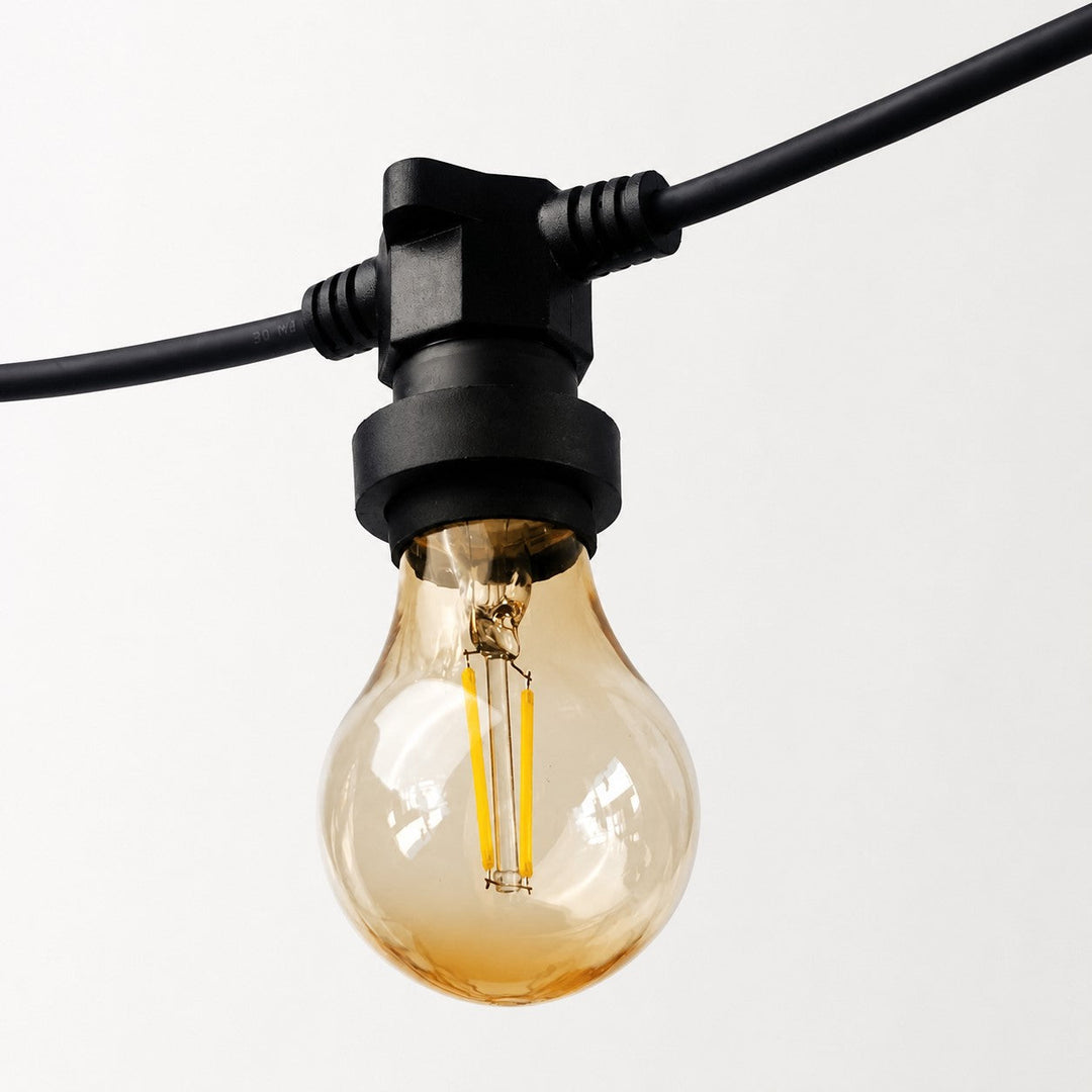 A single amber glass globe light bulb hanging from a black outdoor string light connector on a black cable, shown against a plain light gray background.