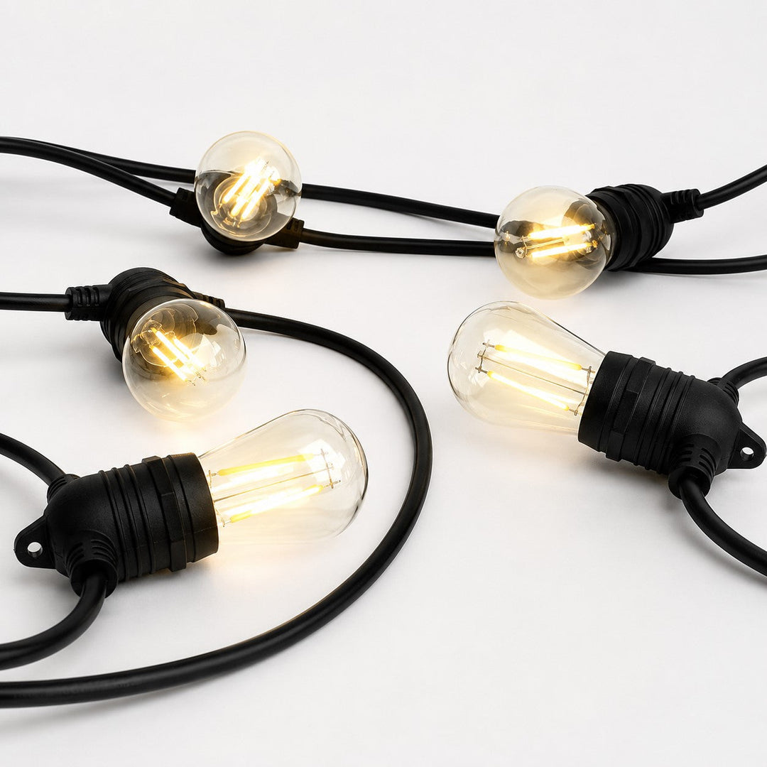 A set of outdoor string lights with clear glass globe bulbs and black cords, shown illuminated on a clean white background.