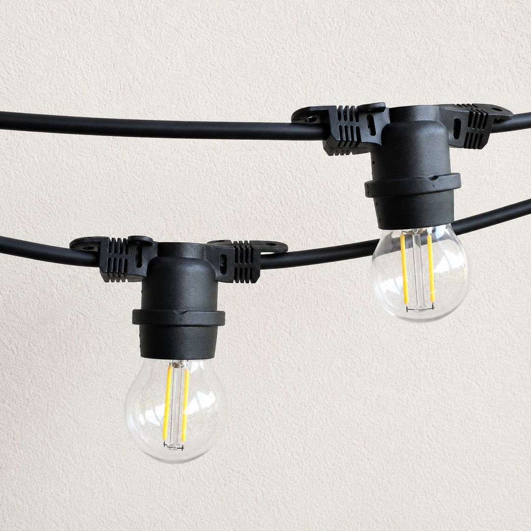 Black string light bulbs with clear glass sockets and visible filament, mounted on a black cable against a light beige textured wall.