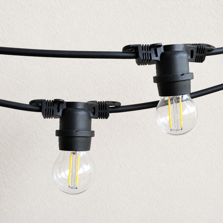 Black string light bulbs with clear glass sockets and visible filament, mounted on a black cable against a light beige textured wall.